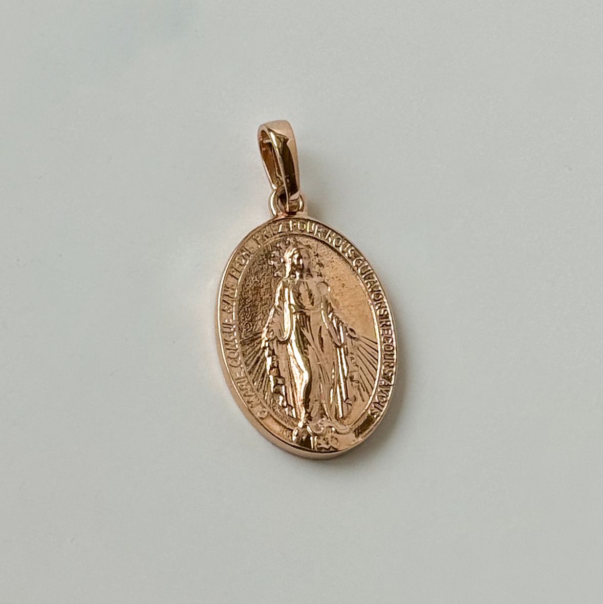 Rose gold pendant with a religious design on a light gray background