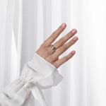 Hand wearing a silver ring with pink nail polish against a white background
