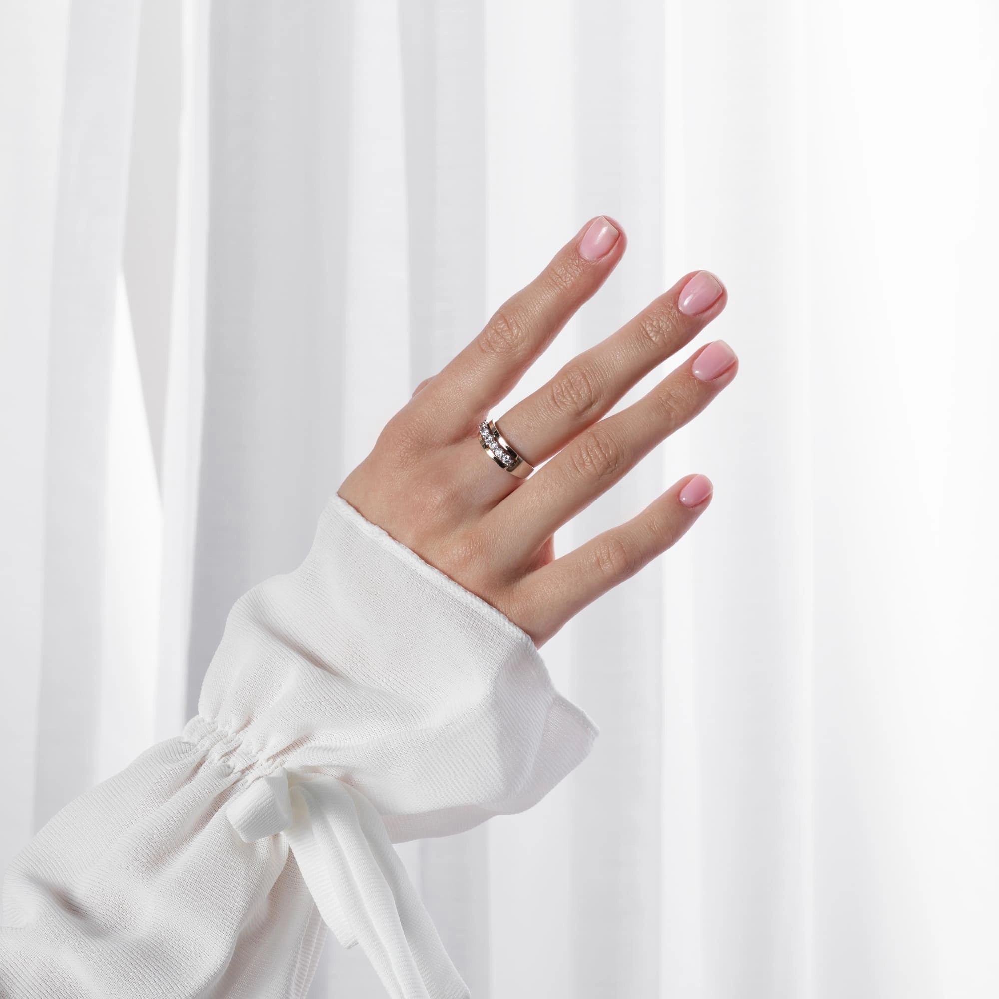 Hand wearing a silver ring with pink nail polish against a white background