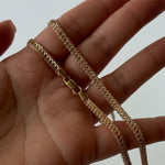Gold chain held in a hand against a neutral background