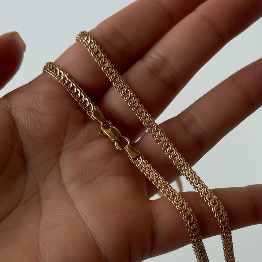 Gold chain held in a hand against a neutral background