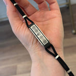 Hand holding a black braided cord with metallic accents