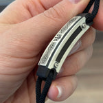 Hand holding a black and silver bracelet.